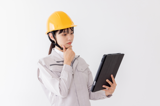 タブレットを使用しながら悩む作業服の女性